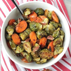 Roasted brussels sprouts and carrots in maple syrup and mustard glaze in a bowl with a spoon.