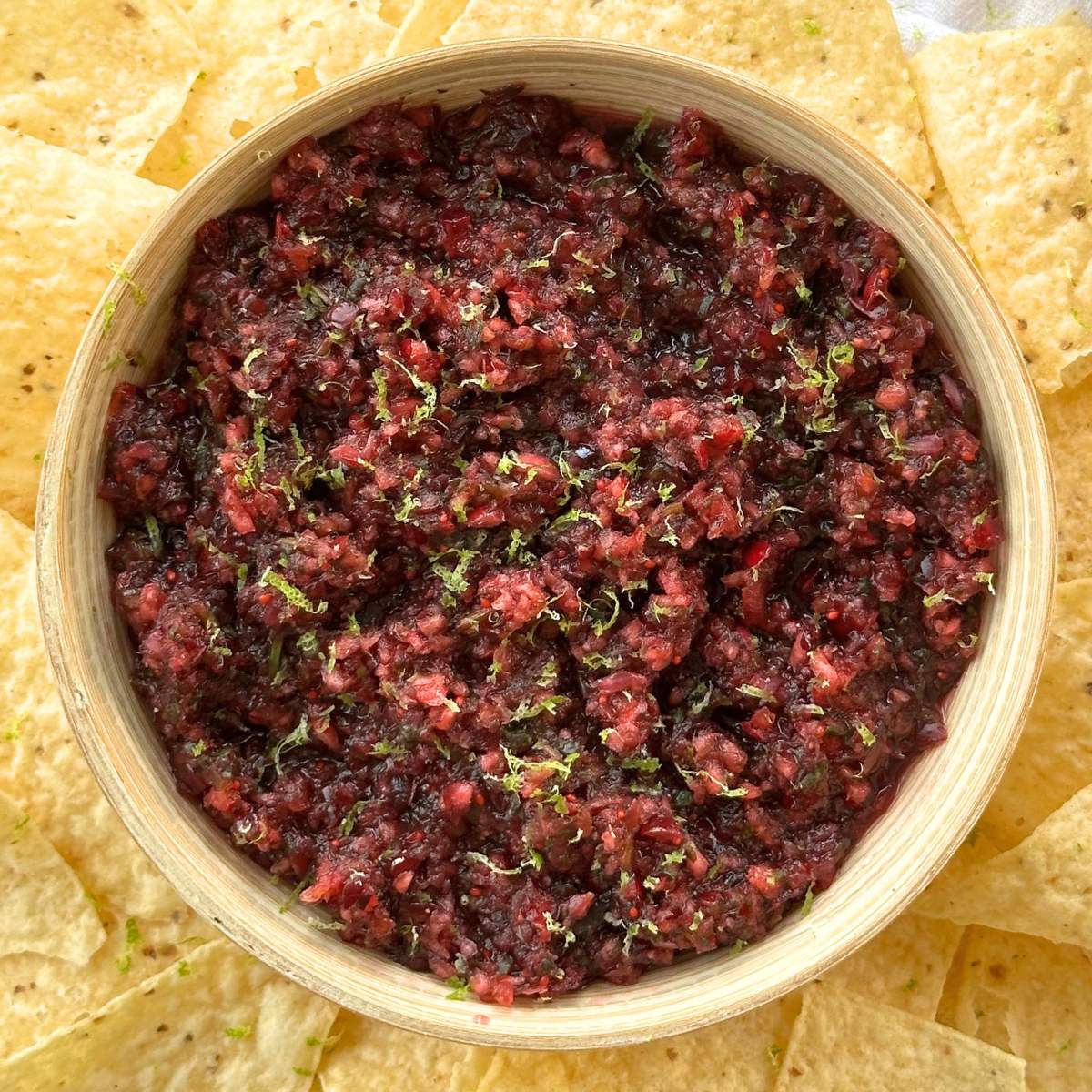 Cranberry salsa in a bowl with lime zest on top and chips around the bowl.
