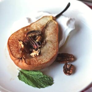 Roasted pear with maple and pecans on top of coconut whipped cream on a plate.