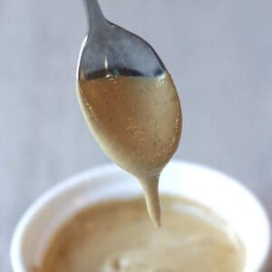 Vegan cashew queso dripping from a spoon into a bowl with more cip.