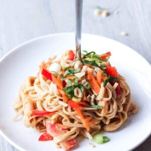 Vegan thai peanut noodle salad piled on a plate with a fork in the center.