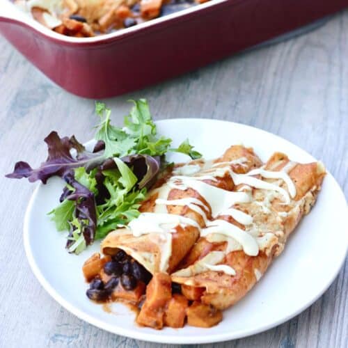 Sweet potato black bean enchiladas on a plate with a casserole dish behind it.