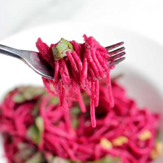 Fork holding noodles coated with beet pasta sauce.