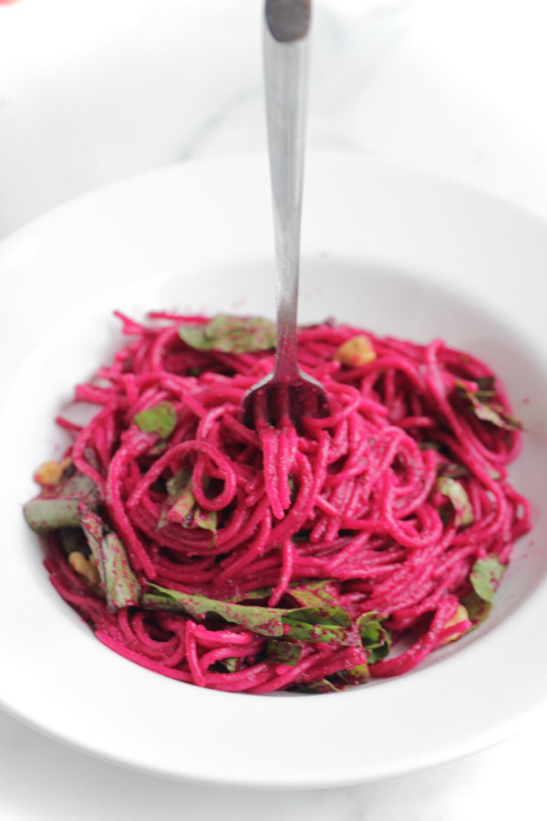 Pasta with beet sauce in a white bowl and a fork in the middle