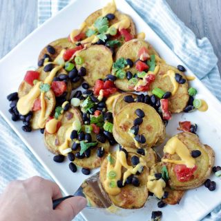 Platter of vegan potato nachos are loaded with creamy queso, beans, tomatoes and green onion.