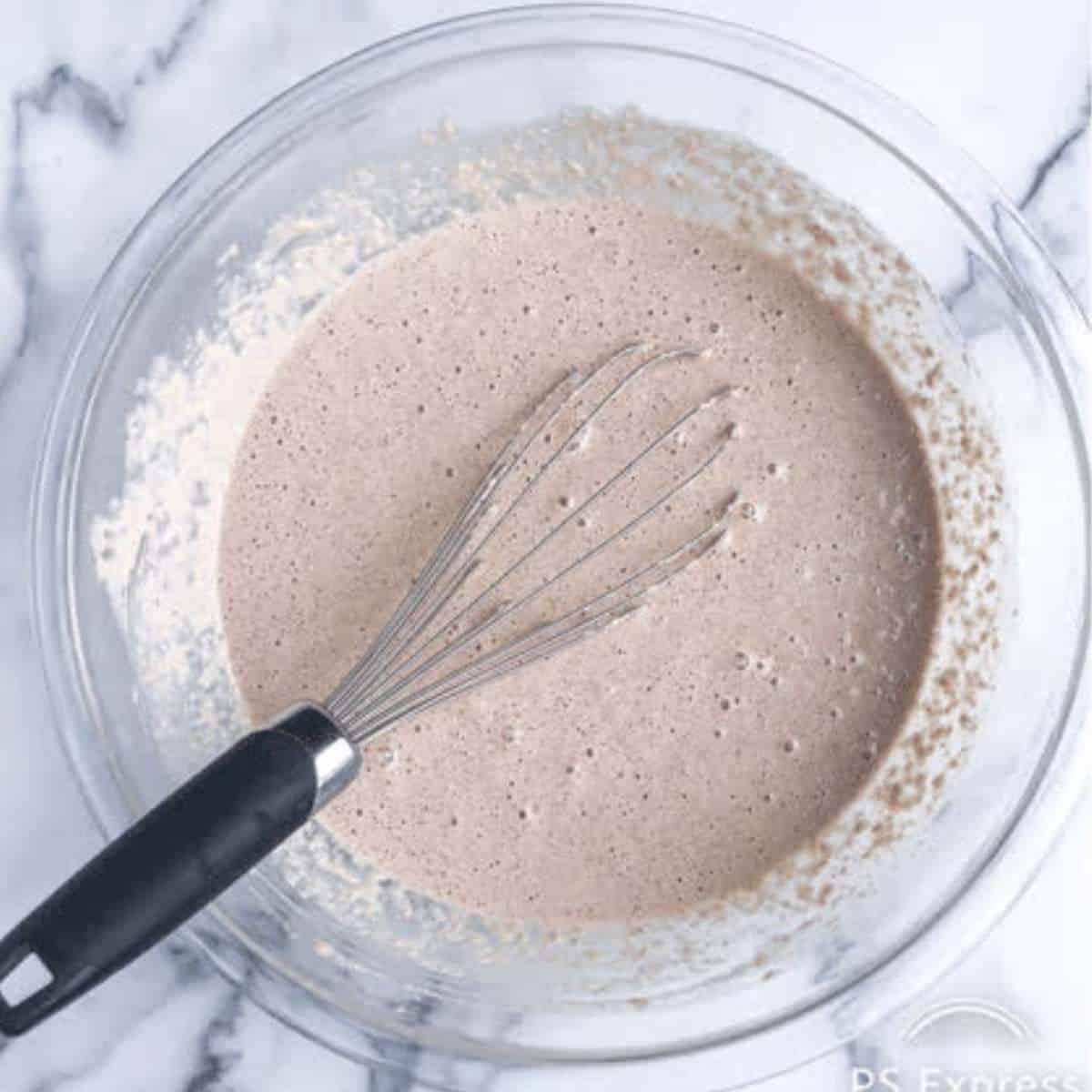 Batter to make gluten-free vegan oat flour waffles in a bowl with a whisk.