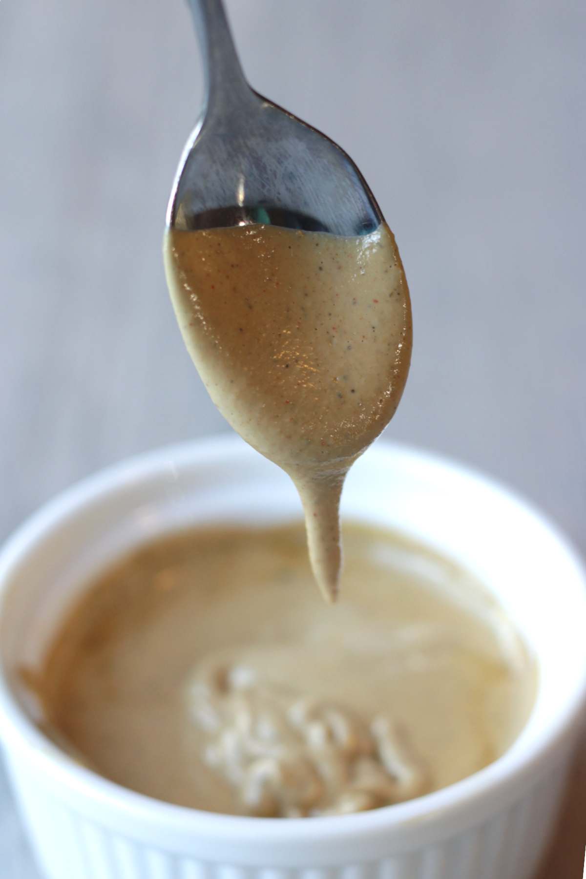 Vegan cashew queso dripping from a spoon into a bowl full of it below.