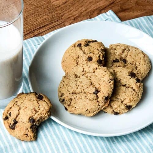 Vegan, gluten-free chocolate chip cookies on a plate next to a glass of milk with one on the side with a bite taken.