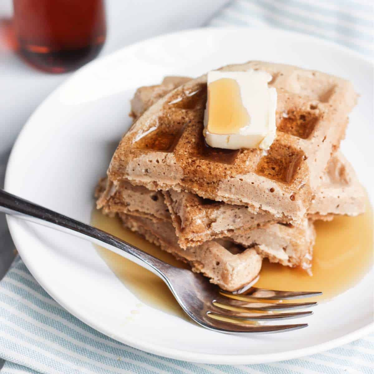 Gluten-free vegan oat flour waffles stacked on a plate with butter and syrup on top. 