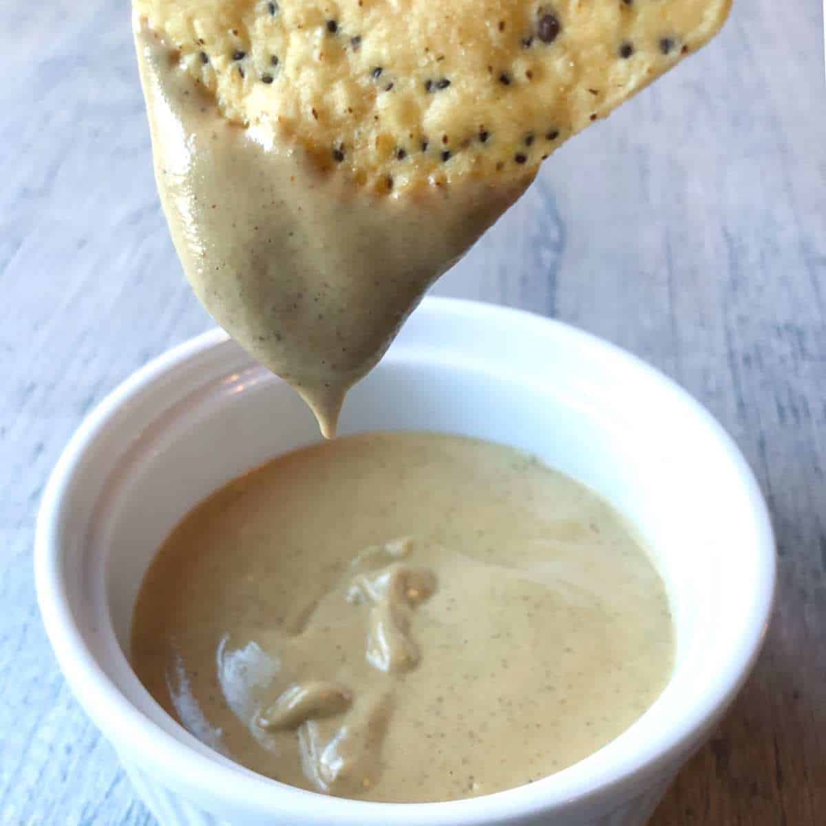 Vegan cashew queso on a chip dripping into a bowl with the dip.