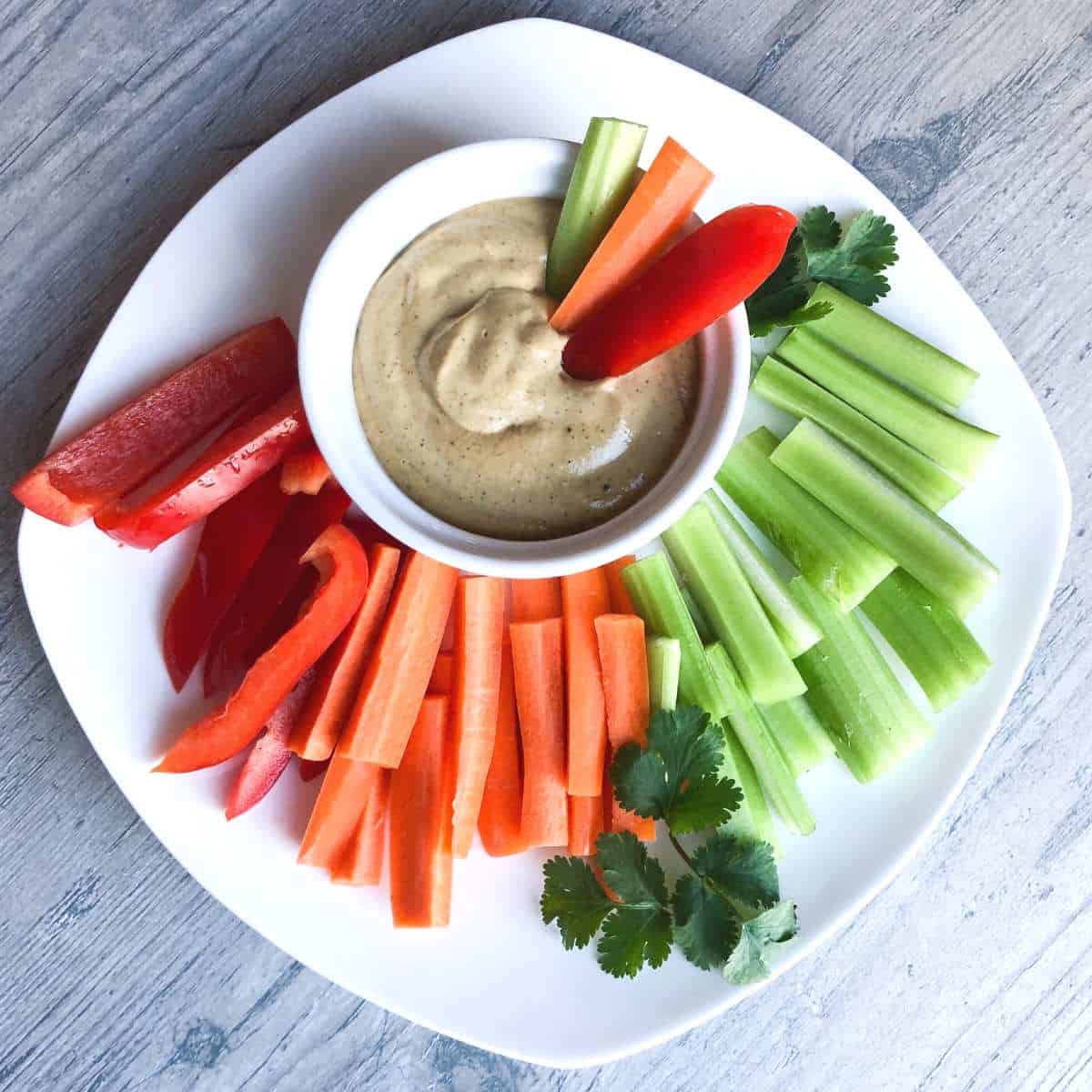 Vegan cashew queso dip on a platter with celery and pepper strips.