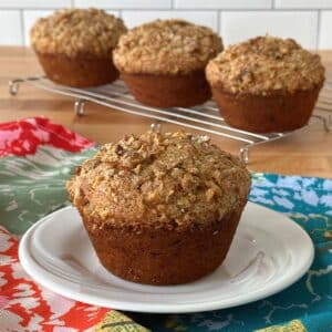 Jumbo banana muffin on a white plate with floral napkin with 3 muffins in background.