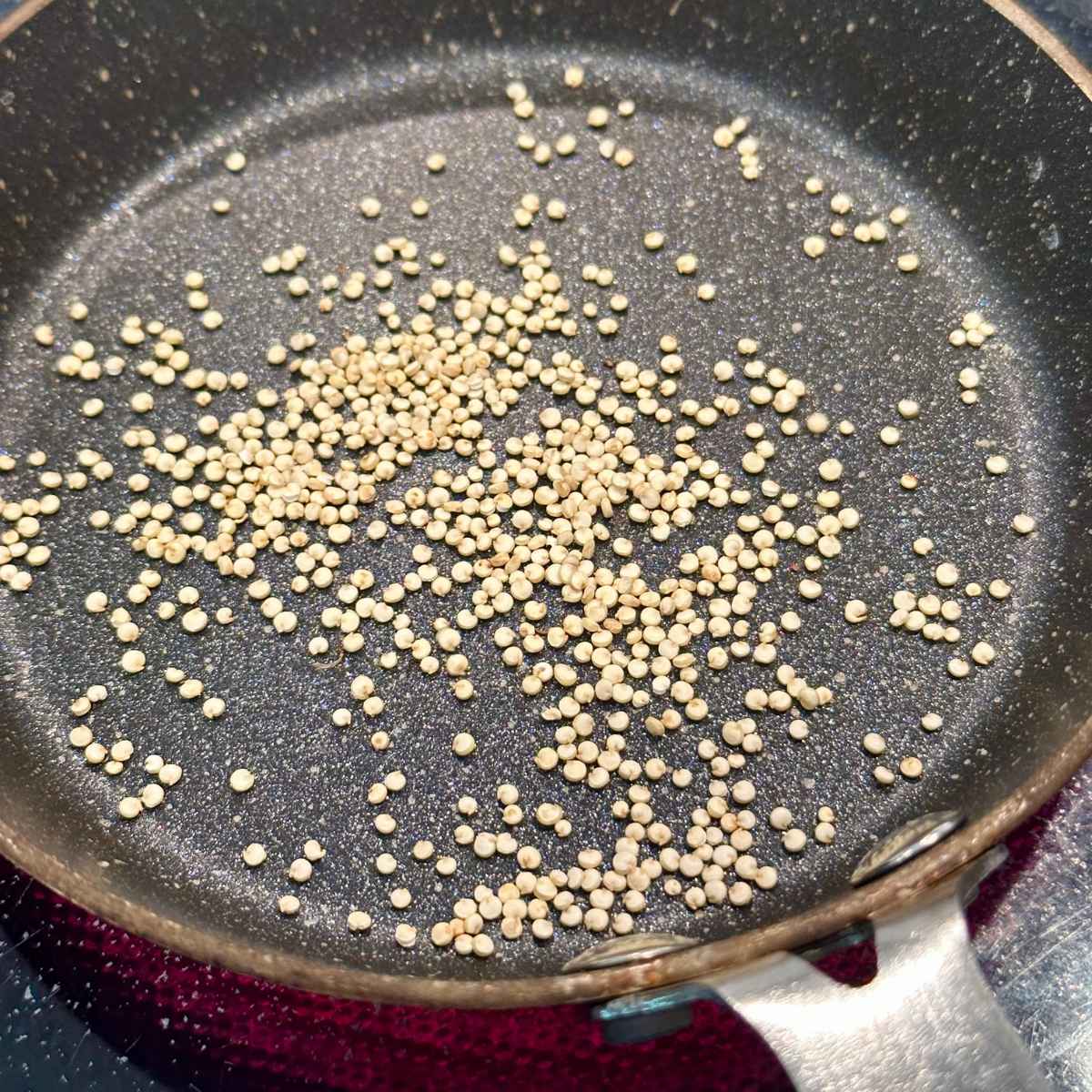 Quinoa toasting in small 5.5" granite pan on stove. Burner is red underneath the pan.