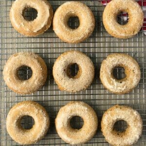 9 gluten-free vegan apple cider donuts on a wire rack on top of a wood background.