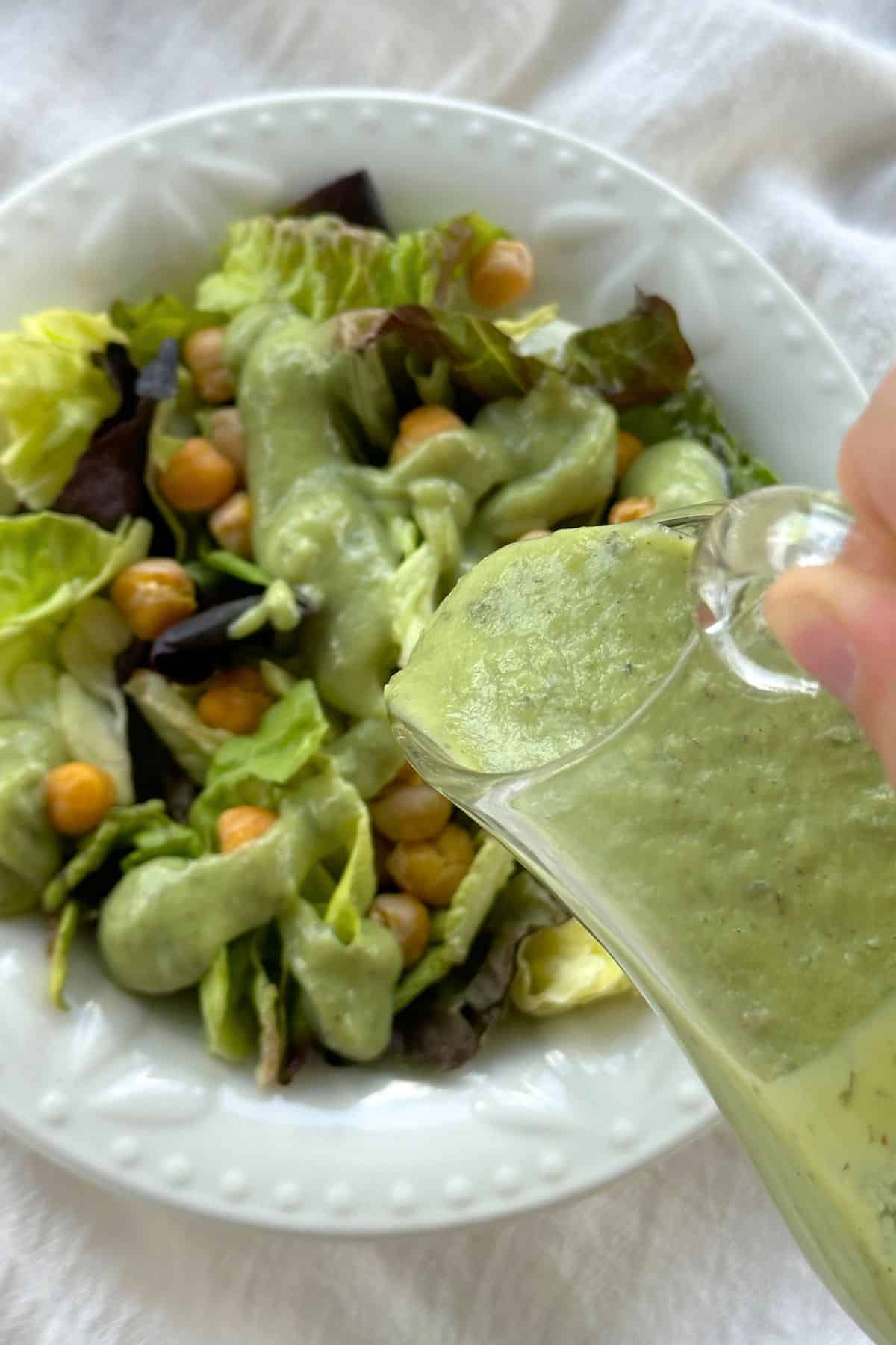 Vegan avocado ranch dressing being poured on top of a salad with green and red lettuce and roasted chickpeas.