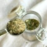 Half a teaspoon of dairy-free ranch seasoning with small glass jar of dry seasoning mix in the background.