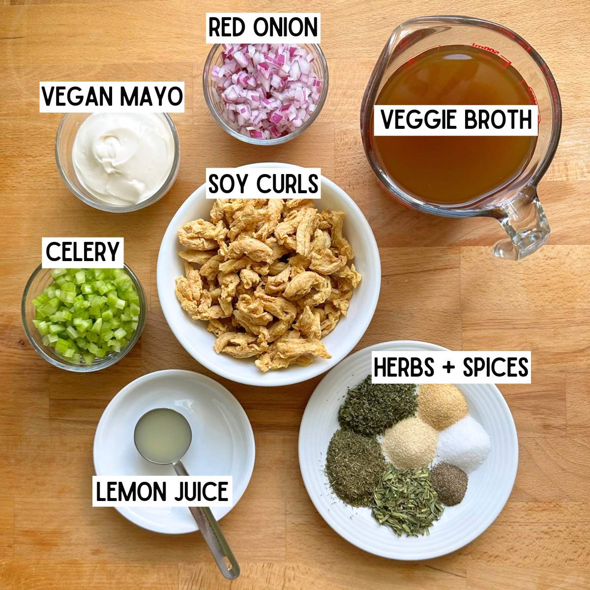 Ingredients to make vegan chicken salad with corresponding written labels: vegan mayo, red onion, veggie broth, celery, soy curls, lemon juice, herbs, and spices.