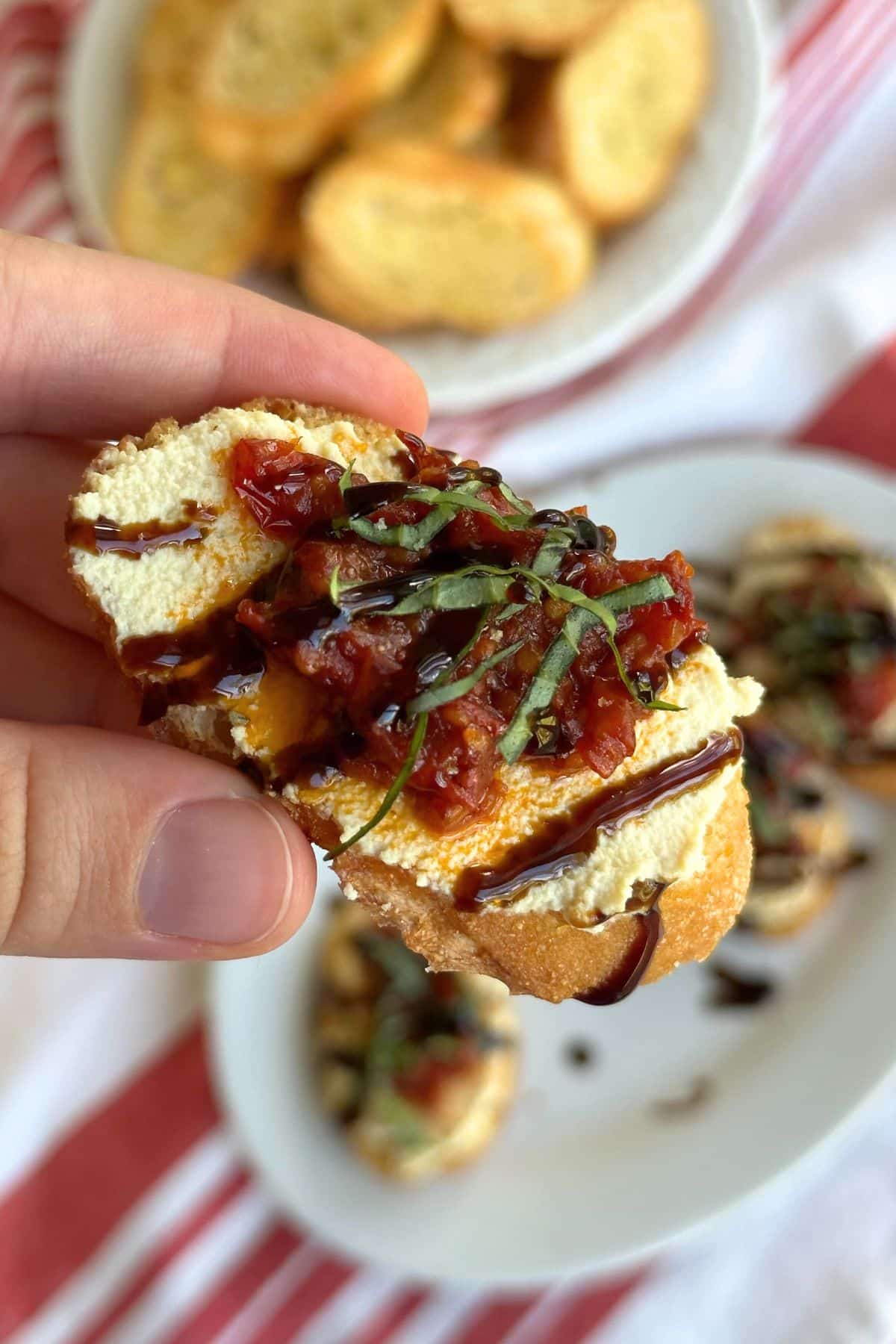 Crostino with tofu ricotta, jammy tomato confit, basil chiffonade, and balsamic glaze. More vegan crostini appetizers are in the background.