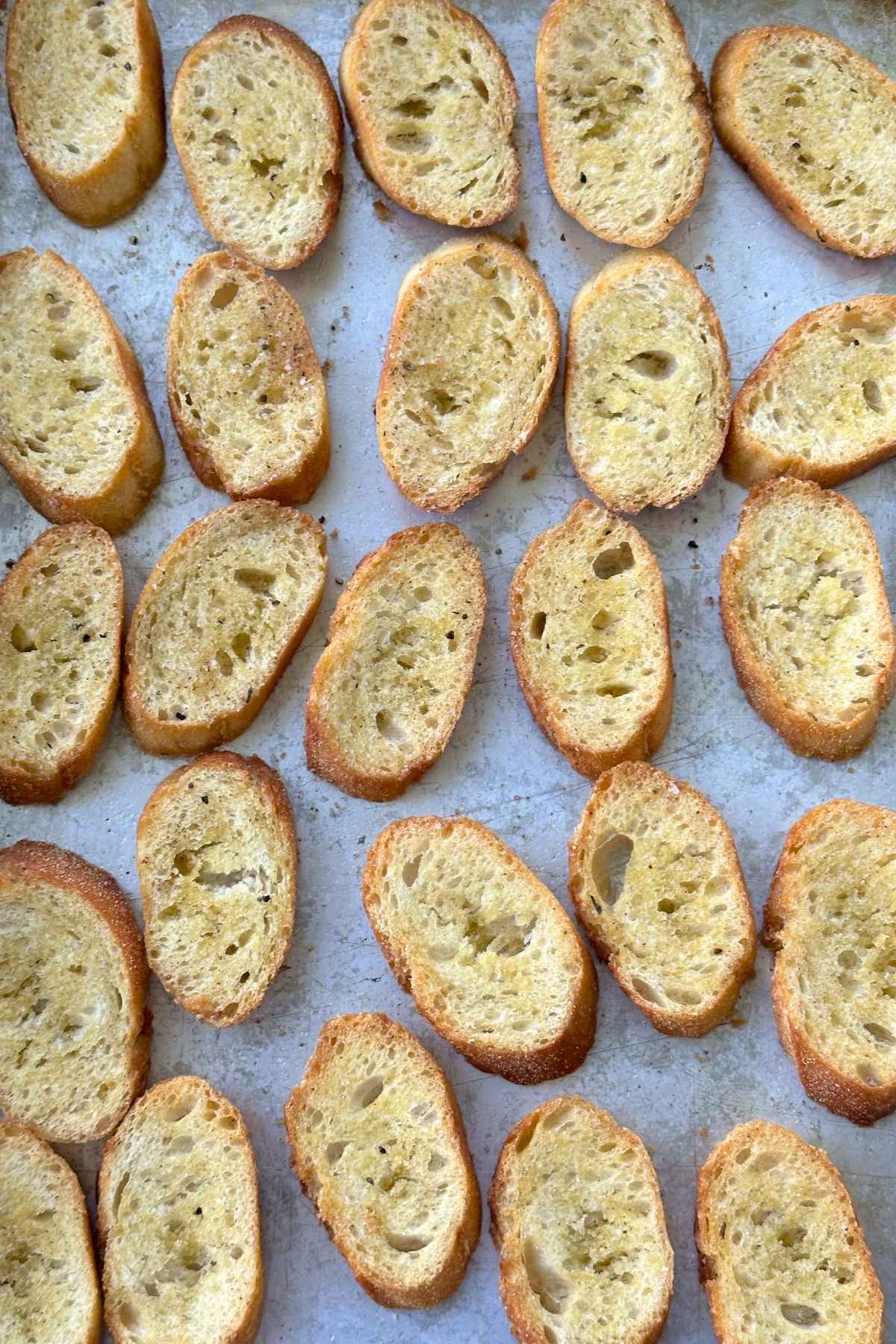 Baked crostini laying flat on a baking sheet.