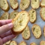 Crostini held by a hand with a baking sheet with more crostini in the background.