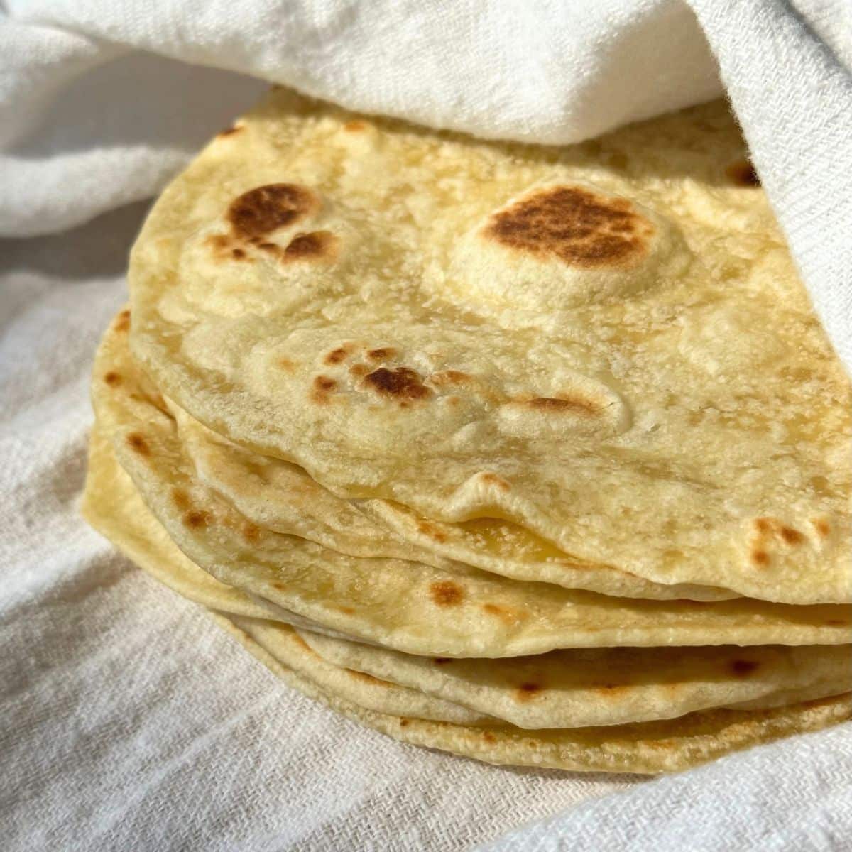 Homemade vegan flour tortillas stacked and wrapped inside a white cloth napkin.