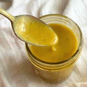 Maple Dijon vinaigrette on a spoon dripping into a jar with more of the dressing.