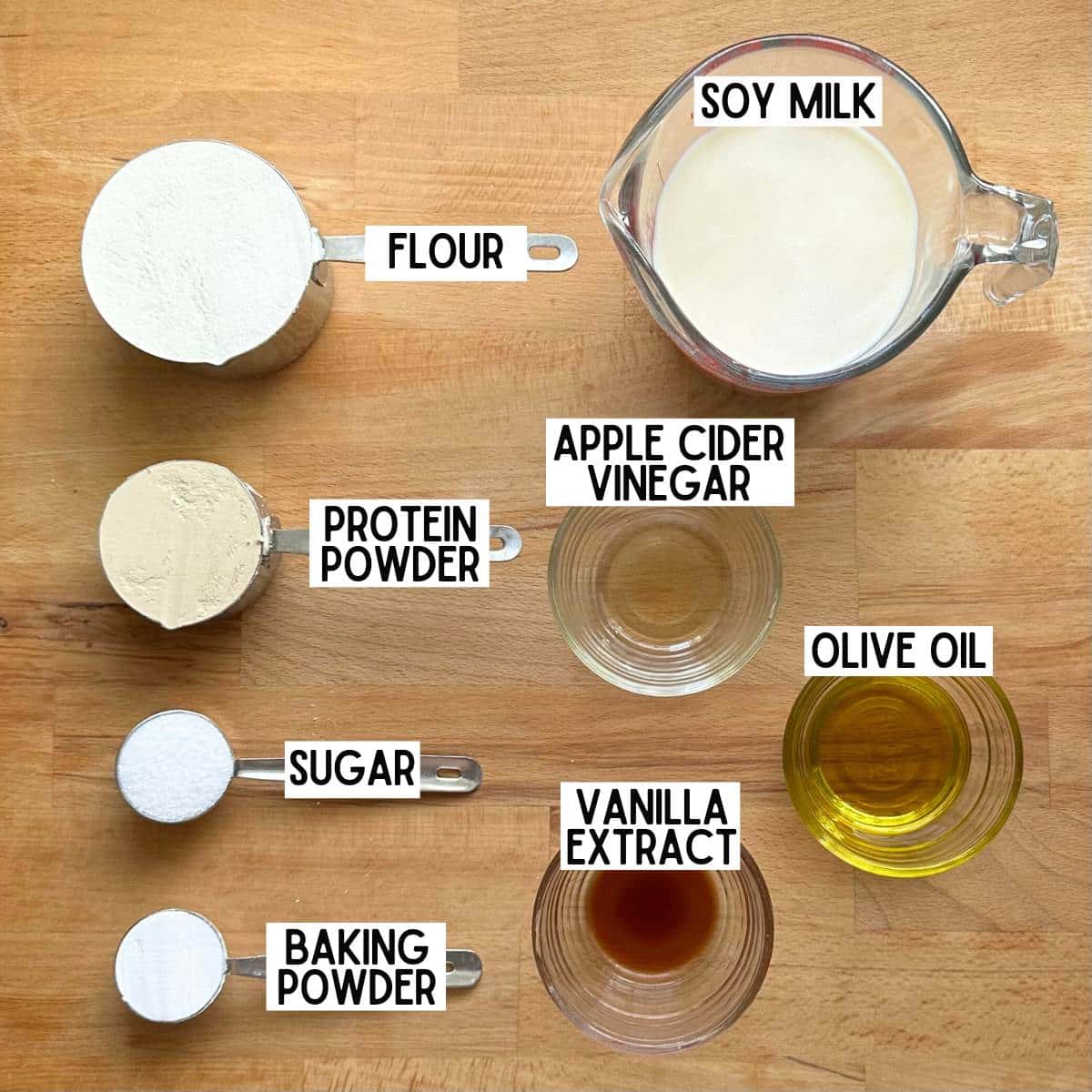 Ingredients to make protein waffles with corresponding labels: flour, soy milk, protein powder, apple cider vinegar, sugar, vanilla extract, olive oil, baking powder.