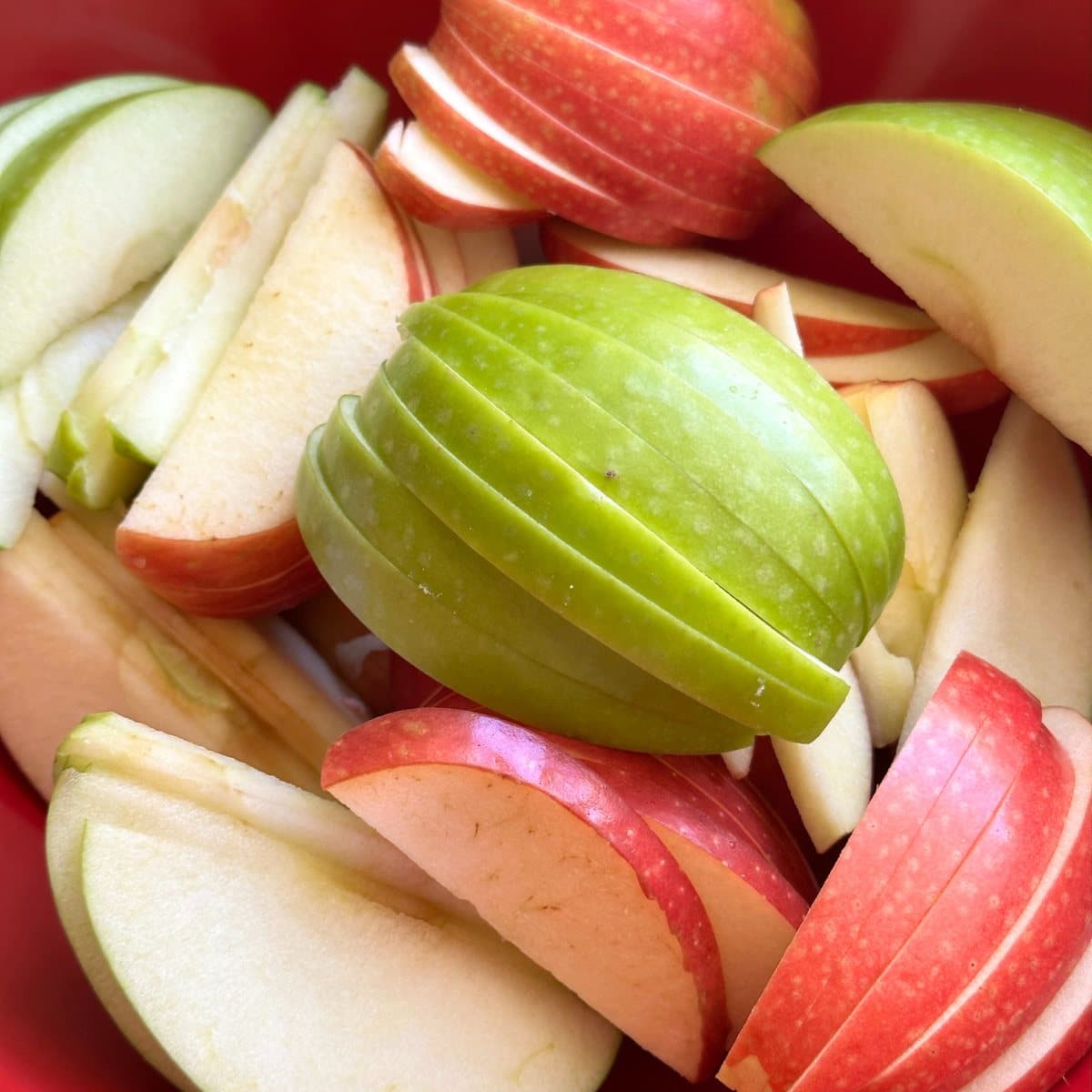 Thin slices of red and green apples in a red bowl.