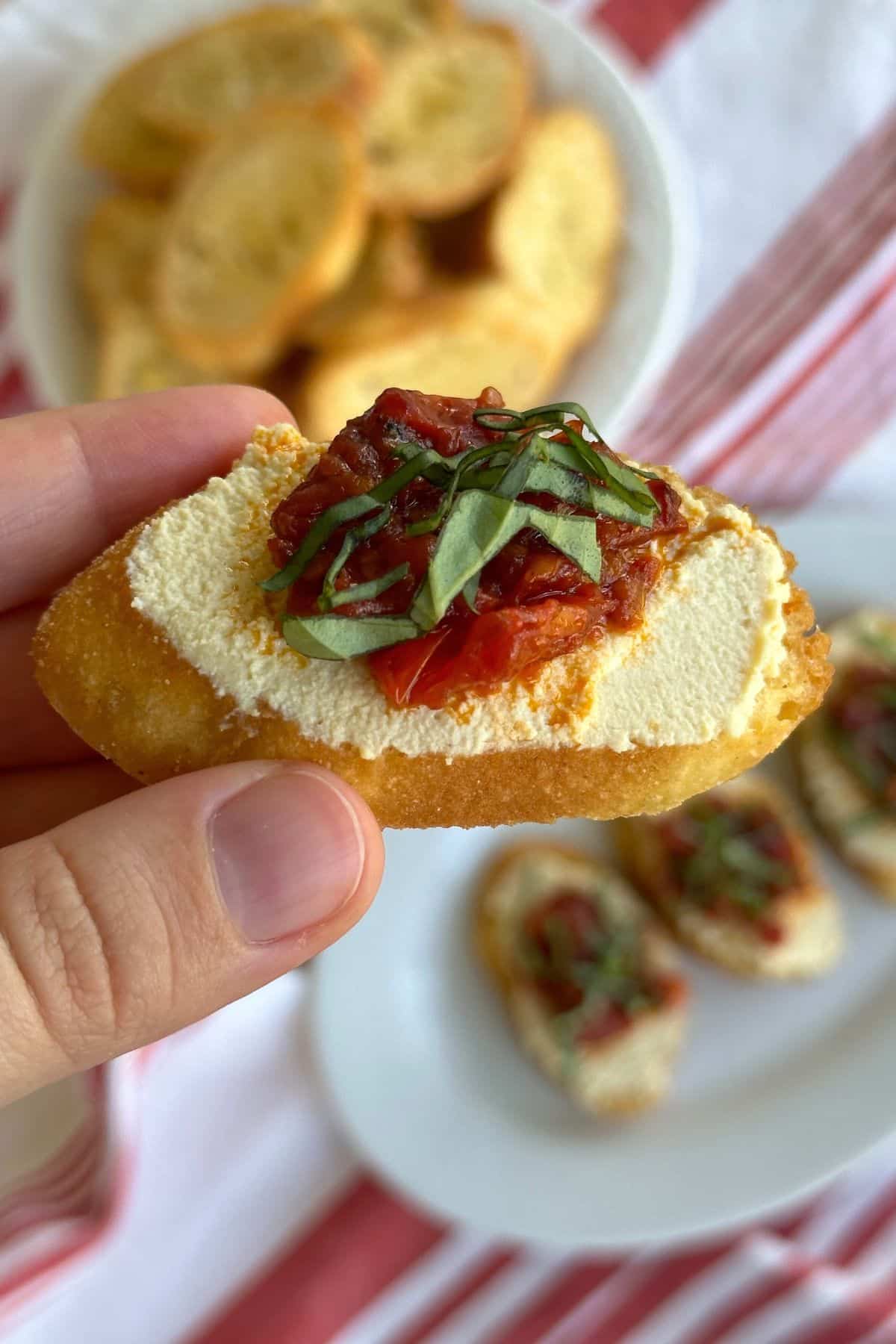 Crostini with tofu ricotta, tomato, and basil topping. In the background are more crostini appetizers.