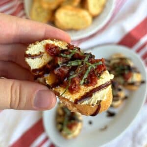 Crostino with tofu ricotta, jammy tomato confit, basil chiffonade, and balsamic glaze. More vegan crostini appetizers are in the background.