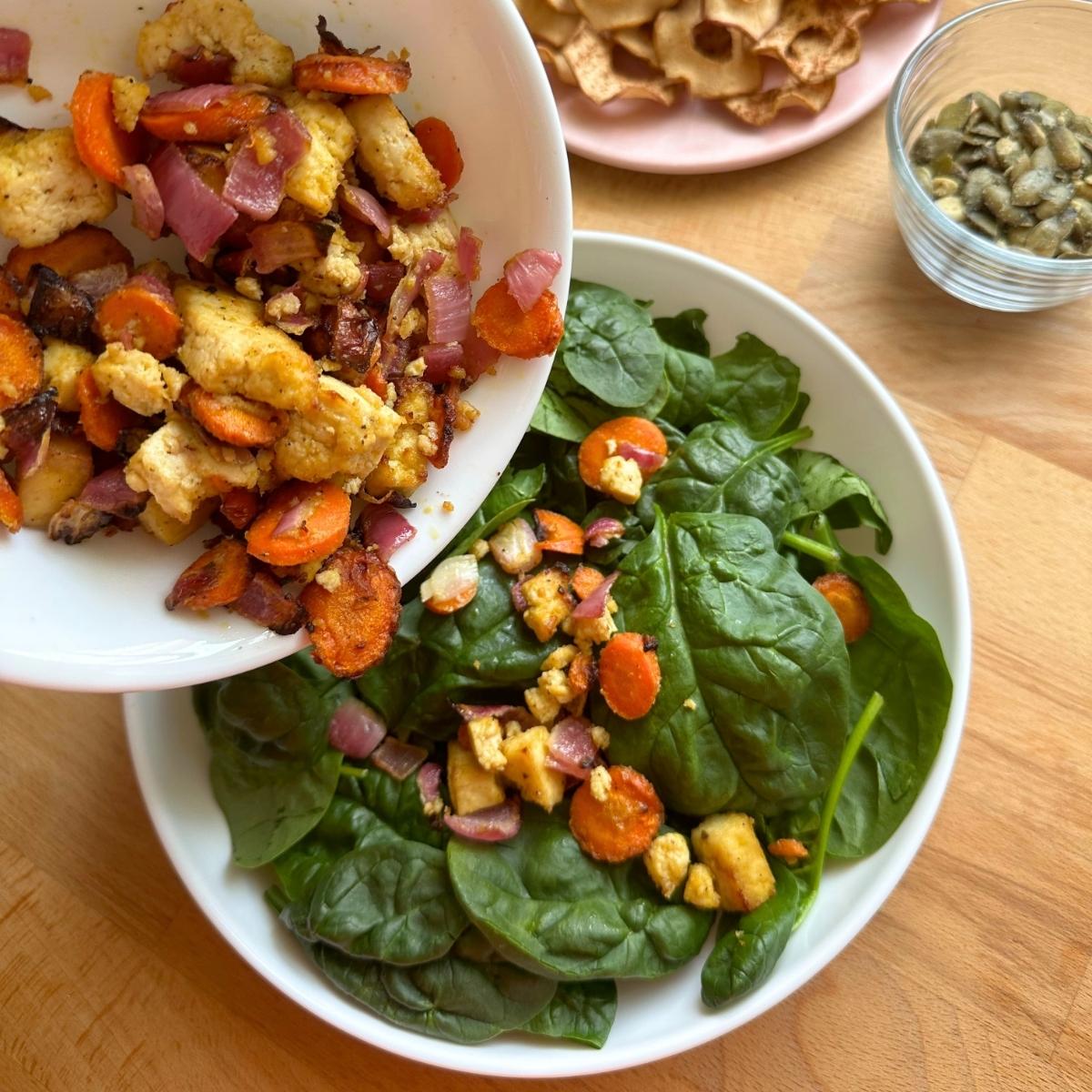 Topping a bowl of spinach with crispy tofu, carrots, and red onions.