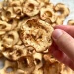 Baked apple chip with cinnamon sprinkled on top with more chips in the background.