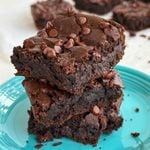 Stack of 3 chickpea brownies on a blue plate with more brownies in the background.
