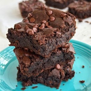 Stack of 3 chickpea brownies on a blue plate with more brownies in the background.