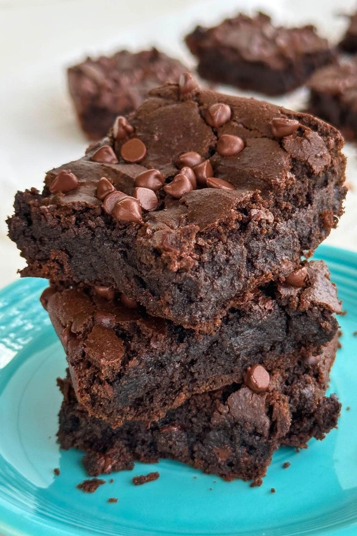Stack of 3 chickpea brownies on a blue plate with more brownies in the background.
