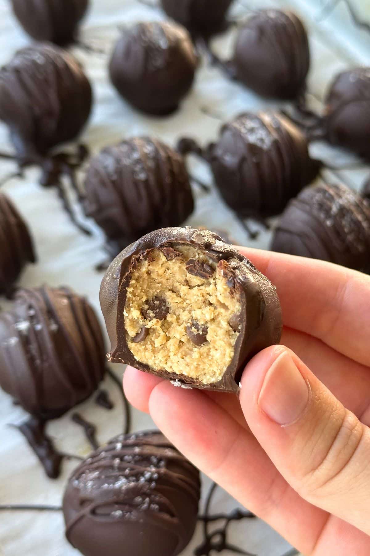 Chocolate covered chickpea cookie dough truffle with a bit taken out of it. The background shows more truffles.
