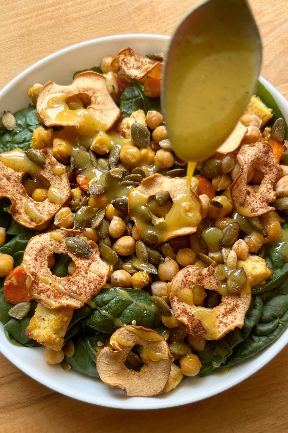 Drizzling maple DIjon vinaigrette over vegan fall spinach and apple salad.