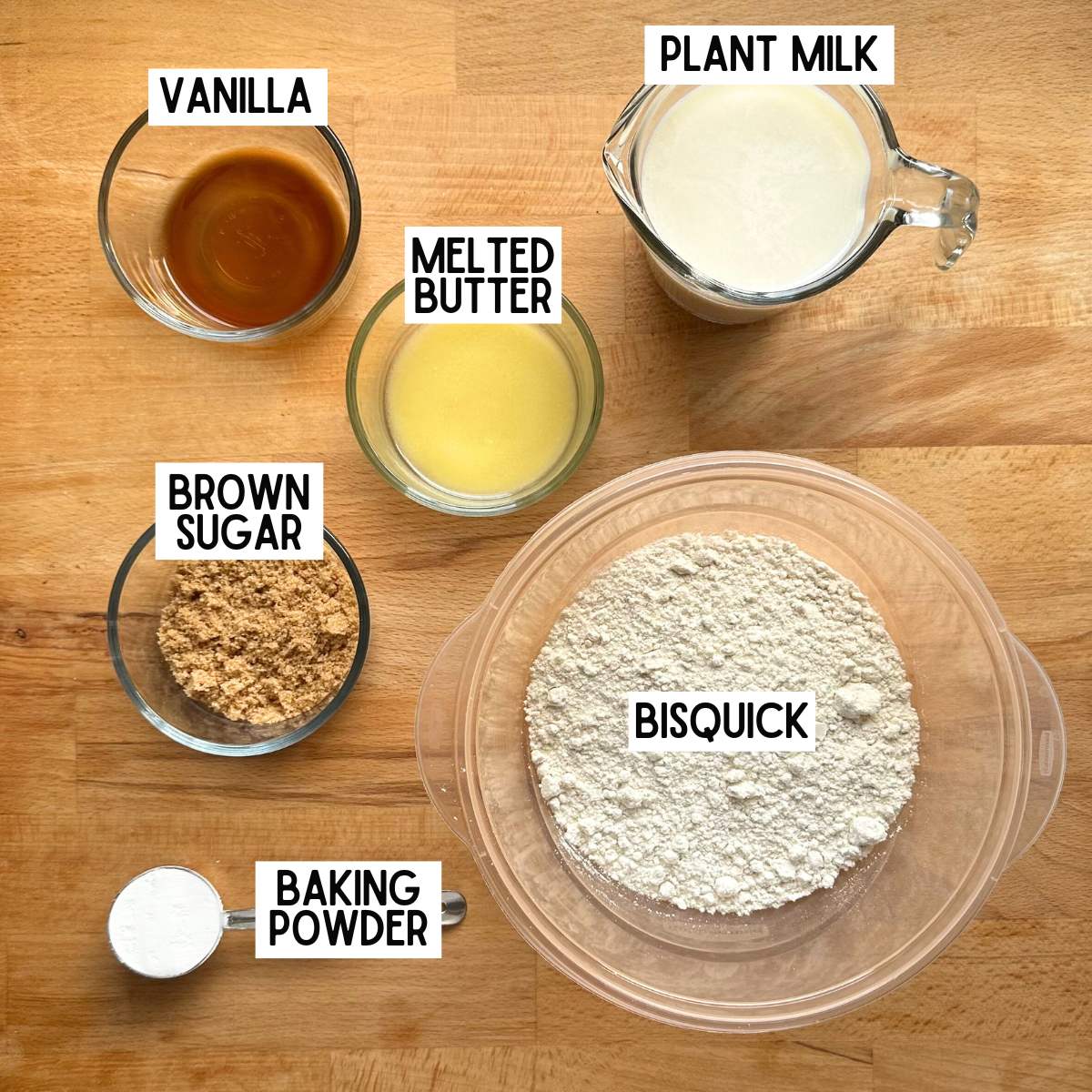 Ingredients to make vegan Bisquick pancakes with corresponding labels: vanilla, melted butter, plant milk, brown sugar, Bisquick, baking powder.