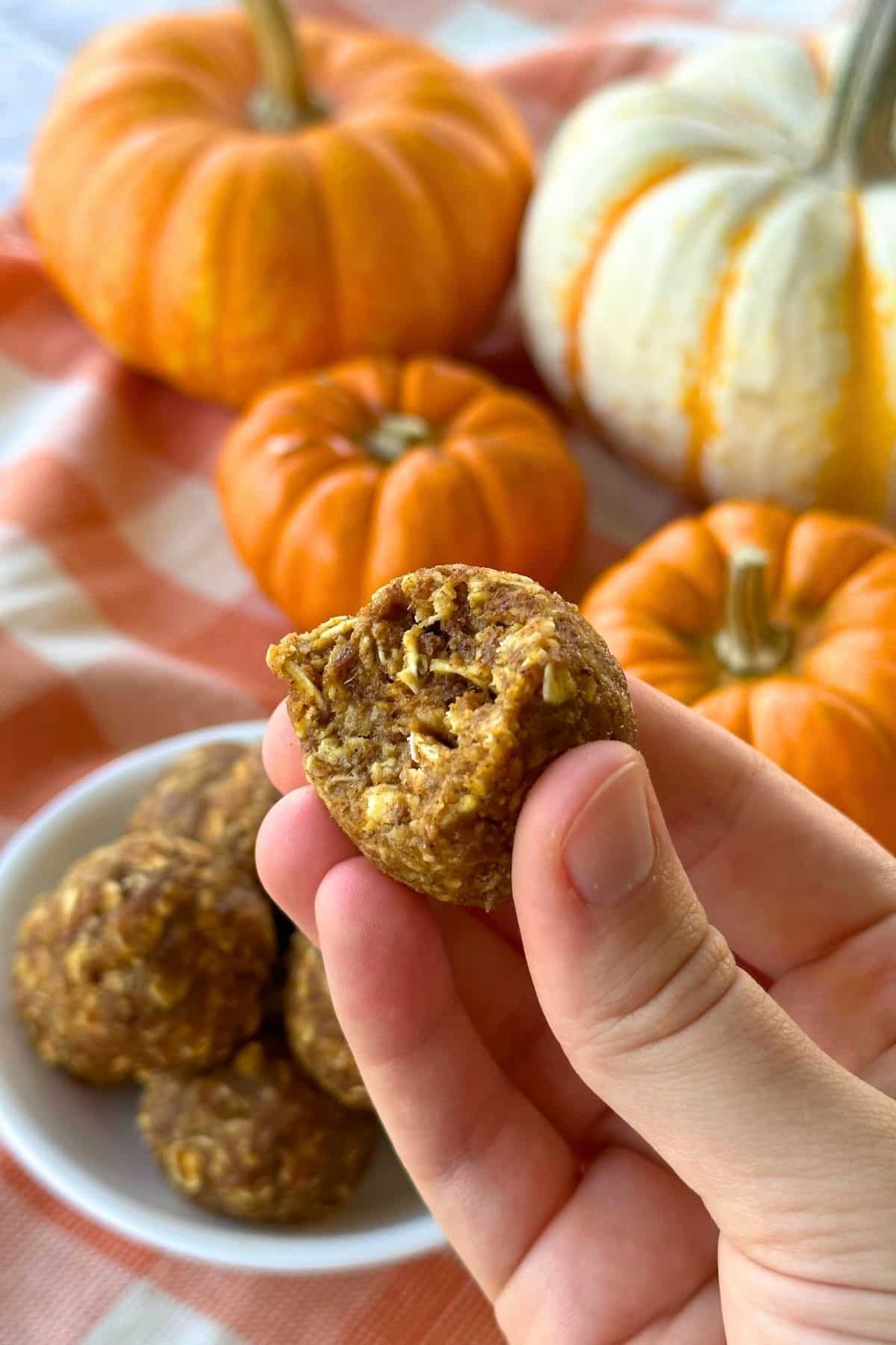 Pumpkin energy ball with a bite taken out of it. More energy bites and pumpkins are in the background.