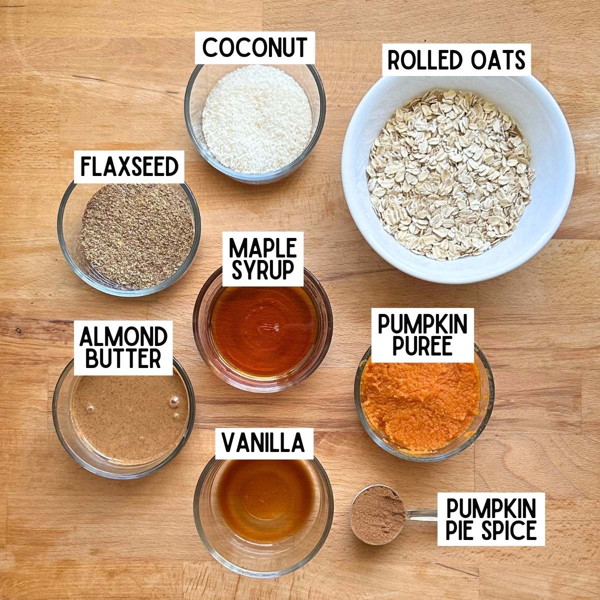 Ingredients to make pumpkin protein balls with corresponding labels: flaxseed, coconut, rolled oats, almond butter, maple syrup, pumpkin puree, vanilla, and pumpkin pie spice.