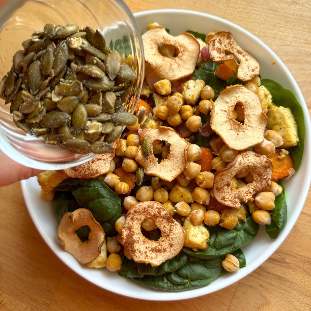 Sprinkling pepitas over vegan fall salad with apple chips and chickpeas.