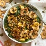 Vegan fall harvest salad in a bowl on top of a white cloth with apple chips and pepitas scattered around.