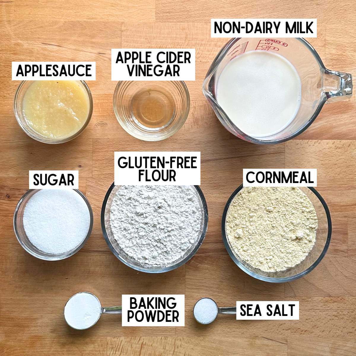 Ingredients to make vegan gluten-free cornbread with corresponding labels: apple sauce, apple cider vinegar, non-dairy milk, sugar, gluten-free flour, cornmeal, baking powder, and sea salt.