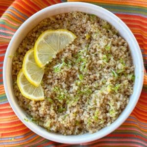 Lemon quinoa in a bowl with lemon slices and lime zest on top of a bright colored napkin.