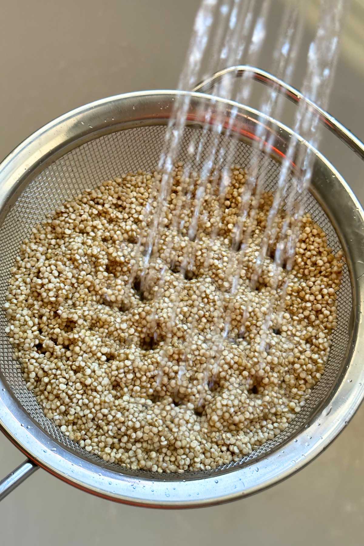 Rinsing quinoa in a fine mesh strainer with water.