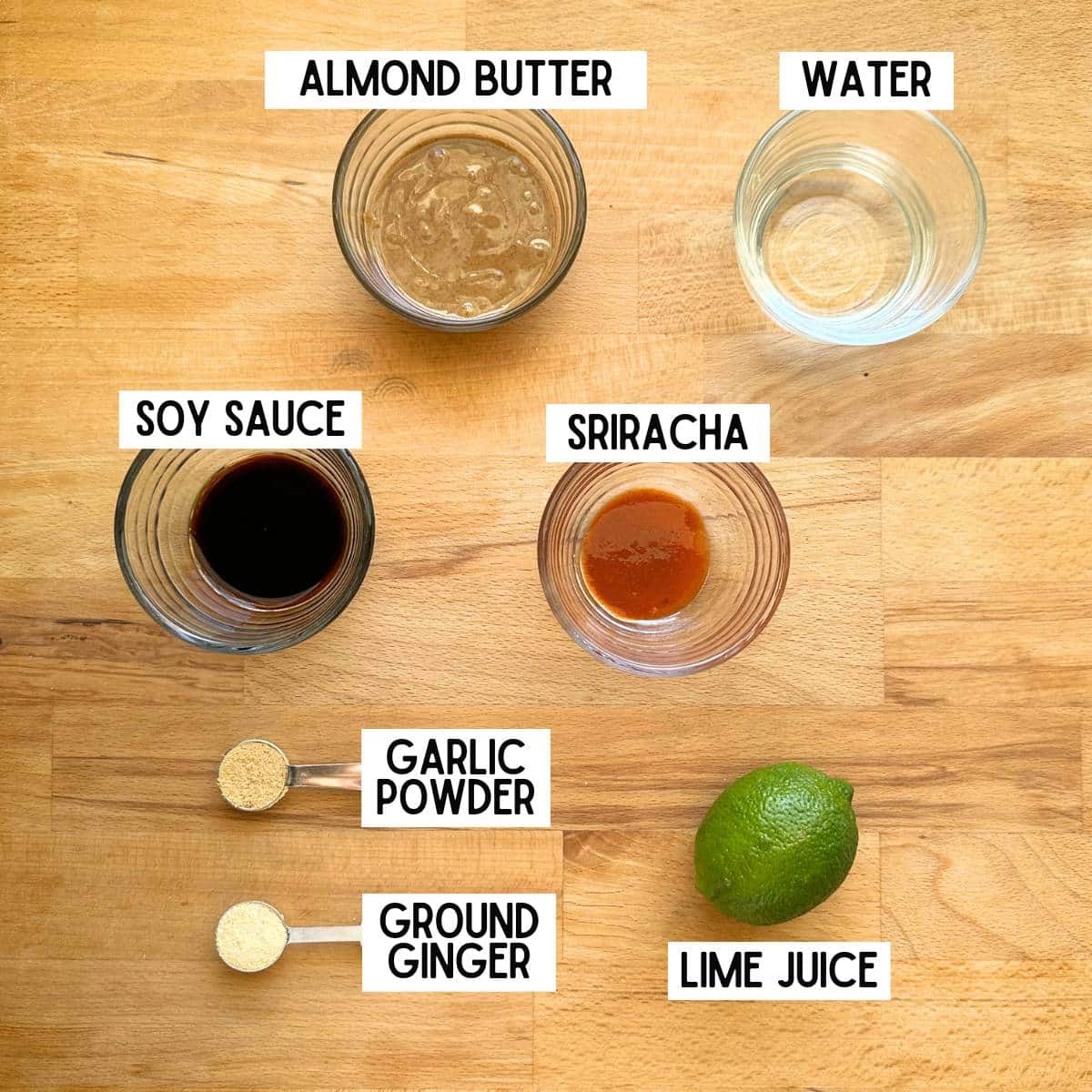 Ingredients needed to make almond sauce with corresponding labels: almond butter, water, soy sauce, sriracha, garlic powder, ground ginger, lime juice.