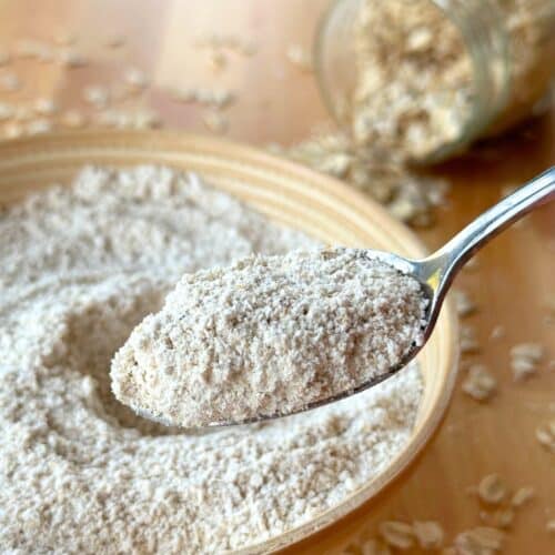 Oat flour on a spoon with more oat flour in the background in a bowl and rolled oats in a jar.