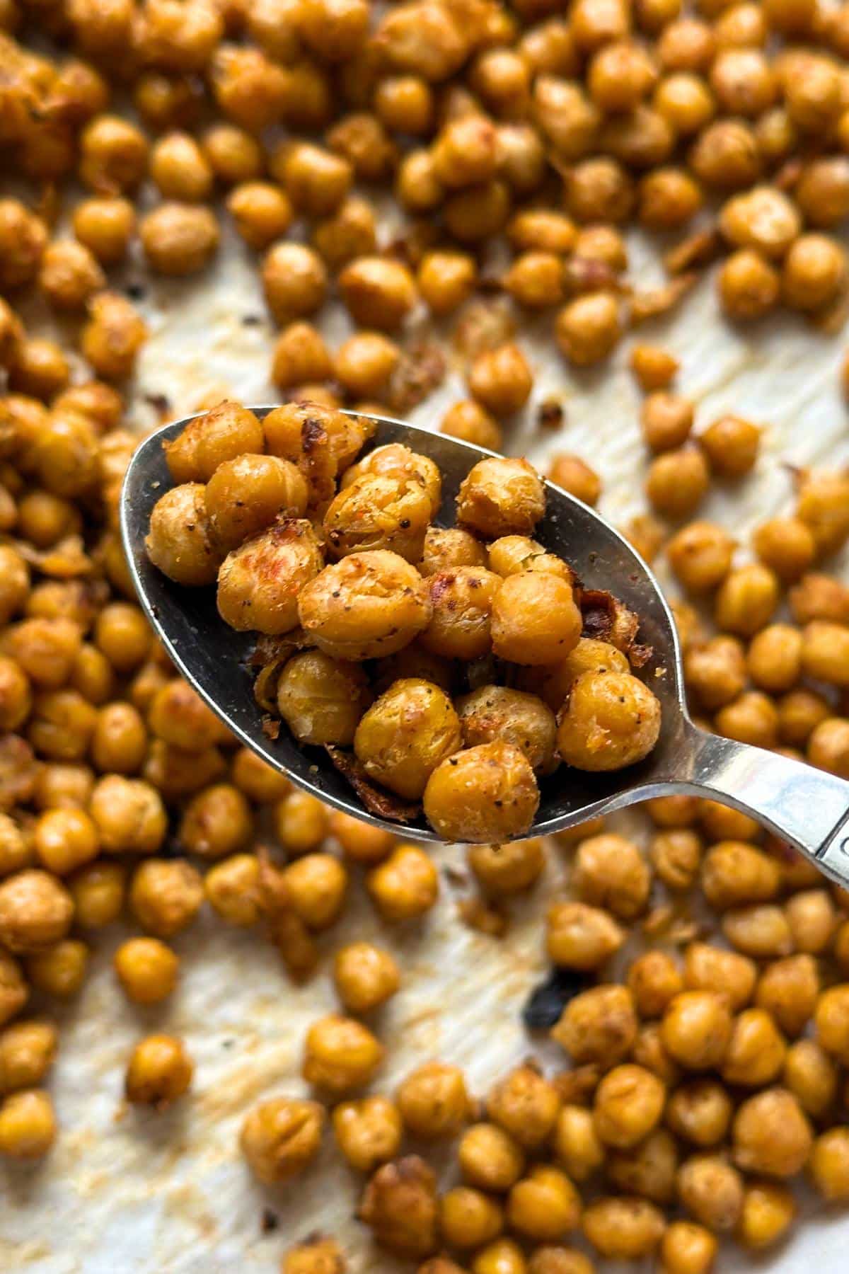 Roasted sriracha lime chickpeas on a serving spoon with more in the background on a pan.