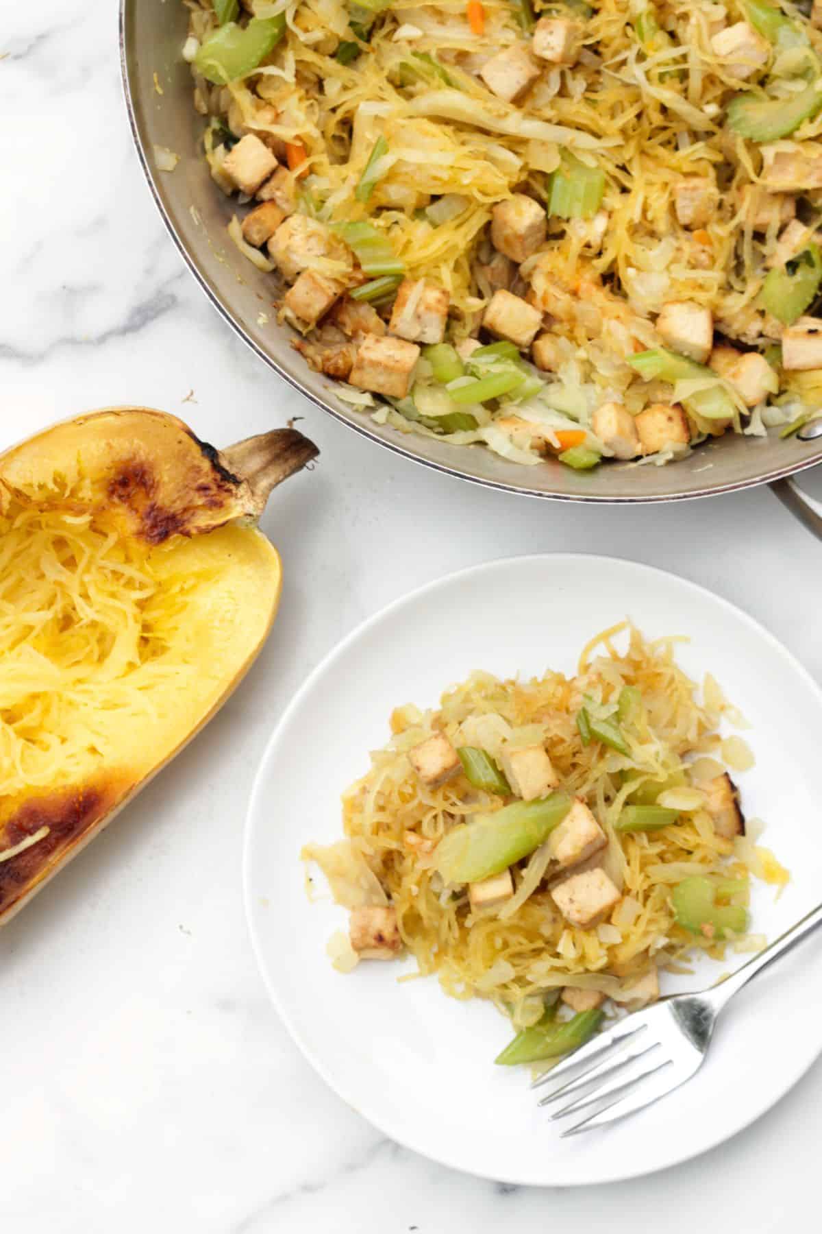 Chow mein on a plate with a spaghetti squash to the side and the pot of more chow mein.