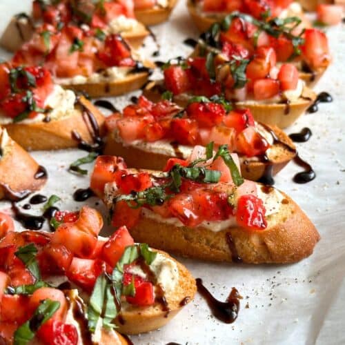 Strawberry balsamic crostini with basil and tofu ricotta in a line on a sheet of parchment paper.